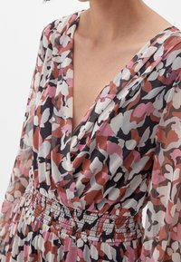 Robe à motif floral avec un décolleté en V profond, des manches longues en dentelle et une taille smockée. Les couleurs incluent le rose, le bordeaux, le blanc et le noir.
