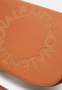 Borsa a tracolla in finta pelle marrone con branding in rilievo e dettagli in stud dorati, dotata di una patta curvata e superficie testurizzata.