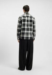 Zwart-wit geblokt flanellen overhemd met een button-down kraag, lange mouwen en een gebogen zoom, gedragen met brede zwarte broeken.