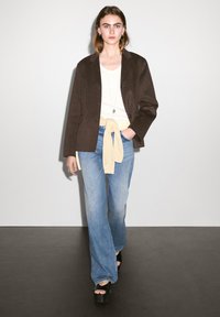 Brown wool blazer over a white t-shirt, light blue wide-leg jeans with a yellow sweater tied at the waist, and black platform sandals.