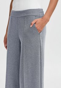 Pantalon de survêtement gris avec une finition texturée. Il présente une jambe large, une taille élastique et une poche latérale. Détails de couture subtils le long des coutures.