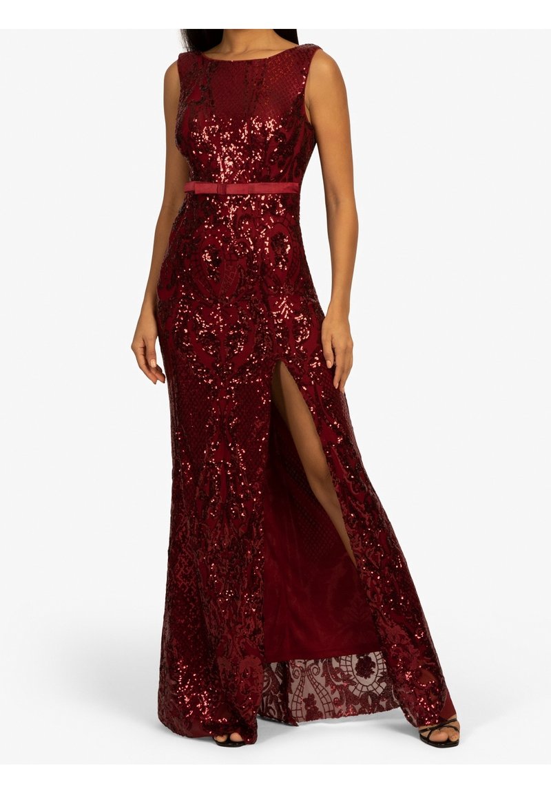 Robe longue bordeaux sans manches à sequins avec motifs floraux, fente haute sur la cuisse et fine ceinture à la taille, portée avec des sandales noires.