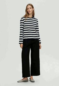 Camisola de manga longa às riscas em azul-marinho e branco, de corte descontraído, emparelhada com umas calças largas pretas e sapatos cinzentos slip-on. Design simples e casual.