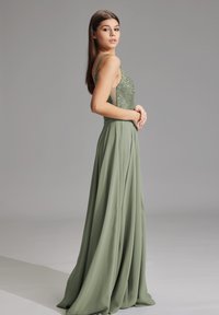 Ärmelloses Abendkleid aus leichtem grünen Chiffon, mit einem glitzernden, mit Perlen besetzten Oberteil und einem fließenden Rock, schräg betrachtet, um die elegante Silhouette zu zeigen.