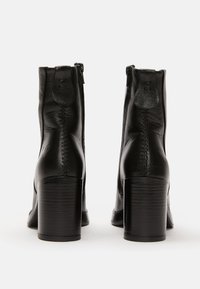 Botas de tobillo de cuero negro con cierre de cremallera, tacones cuadrados, detalles de costura y una textura suave, que exhiben un diseño moderno.