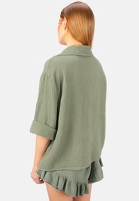 Olivgrünes, zerknittertes Stoffhemd mit kurzen, hochgerollten Ärmeln und einem Kragen, kombiniert mit passenden Rüschenshorts. Rückansicht gezeigt.