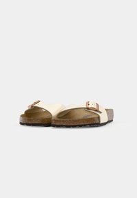 Paire de sandales blanc cassé à bout ouvert avec semelles en liège et boucles réglables en or rose, présentées de face sur fond uni.