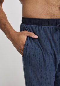 Marineblauwe sportbroek met een gestructureerd verticaal streeppatroon, voorzien van een elastische tailleband en zijzakken.
