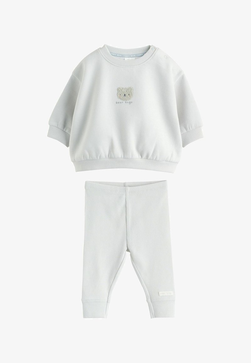 Ensemble pour bébé blanc comprenant un sweat-shirt avec un visage d'ours en peluche et le texte "bear hugs", associé à un pantalon côtelé.