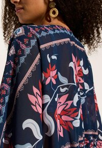 Tessuto trasparente navy a motivo floreale con fiori rosa e rossi, arricchito da un delicato pizzo lungo il colletto e le maniche.