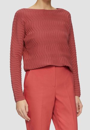 Pull en tricot rouge à texture avec un motif ondulé et des manches longues, associé à un pantalon rouge assorti. Le tissu a un aspect côtelé.