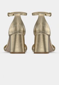 Χρυσά μεταλλικά σανδάλια με χοντρό τακούνι και λουράκι στον αστράγαλο. Λεία υφή, σχέδιο με ανοιχτά δάχτυλα και μινιμαλιστική σιλουέτα.