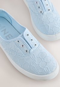 Baskets slip-on bleu clair avec semelles en caoutchouc blanches et broderie florale, dotées d’œillets métalliques sans lacets.