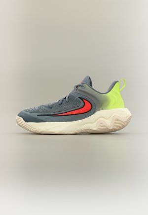 Pelēks un neona zaļš sporta apavu ar sarkanu Swoosh logo, teksturētu zolīšu un šņorējamu dizainu uz neitrāla fona.