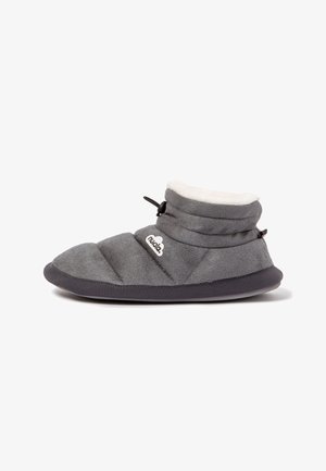 Pantufla acolchada gris con un suave cuello de forro polar blanco, acentos negros y suela de goma, que presenta un logo de marca decorativo.