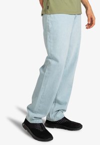 Jean bleu clair en denim, doté d'une coupe décontractée et de jambes droites, associé à des chaussures à enfiler en maille noire avec des accents texturés.