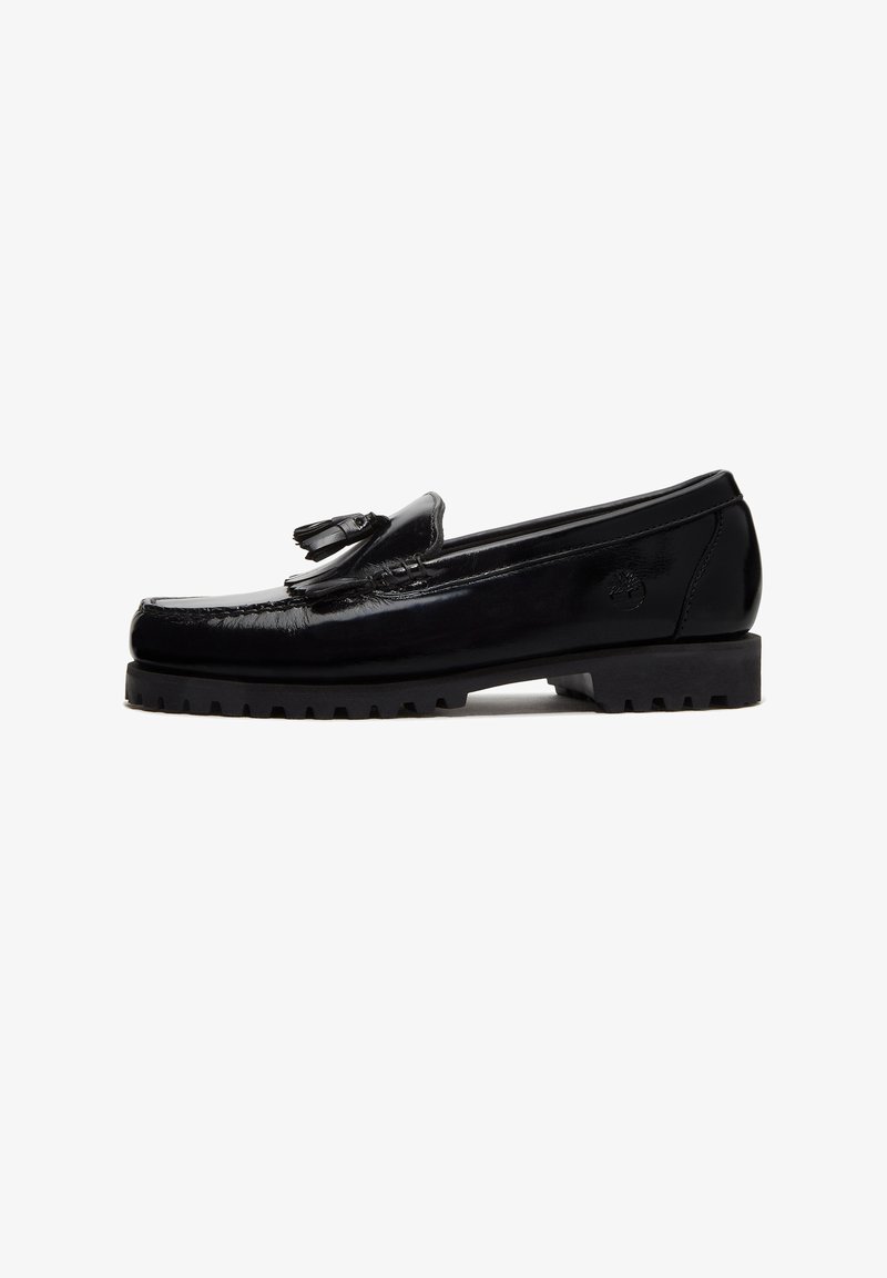 Mocassin en cuir noir avec détail de pompon, semelle épaisse et robuste, et logo embossé sur le côté, présenté de profil sur fond blanc.