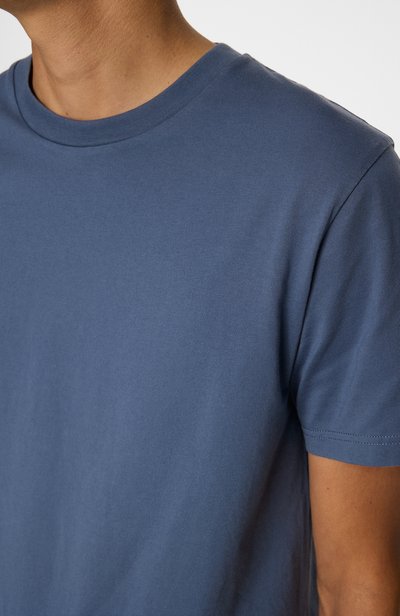 T-shirt à manches courtes, col ras du cou en tissu de coton bleu uni. Texture lisse avec une coupe décontractée et peu de détails de couture.