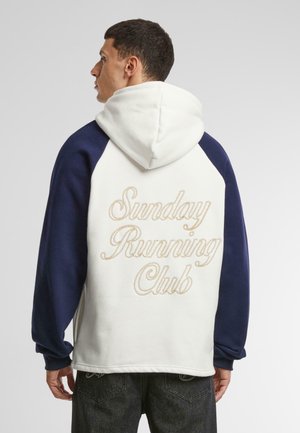 Pullover hoodie in white and navy blue, featuring a hood, raglan sleeves, and "Sunday Running Club" embroidered in gold on the back.