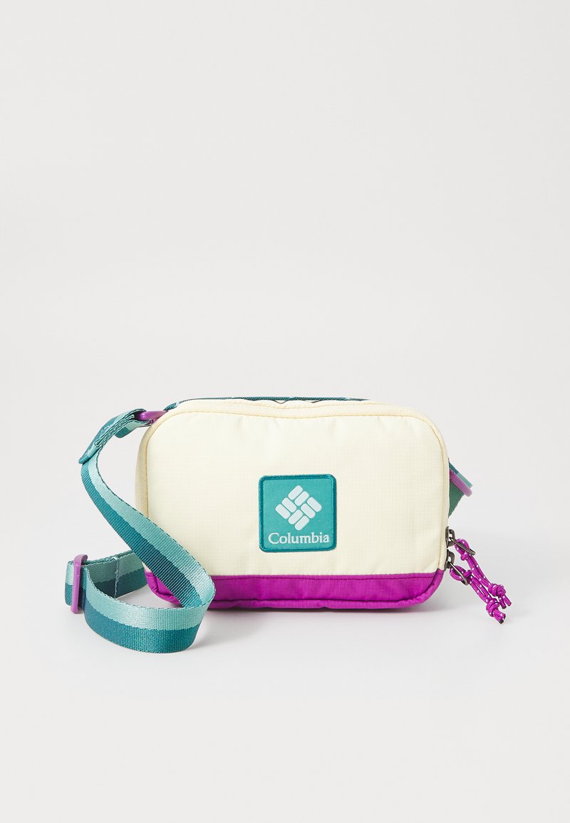 Sac à bandoulière Columbia avec des panneaux crème et violet, doté d'un patch logo en teal, d'une sangle ajustable et d'un tissu texturé. Fermeture éclair avec tirette décorative.