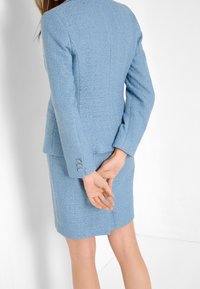 Hellblauer, maßgeschneiderter Anzug aus strukturiertem Stoff. Besteht aus einer taillierten Jacke mit Drei-Knopf-Manschetten und einem knielangen Rock.