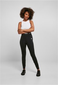 Fekete leggings széles elasztikus derékpánttal, amelyen a "Starter" logó található, fehér ujjatlan toppal párosítva. Sima, rugalmas anyag.