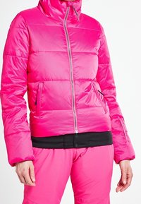 Doudoune fuchsia avec fermeture éclair à l'avant, col haut et deux poches latérales. Le matériau est lisse avec une texture légèrement matelassée.