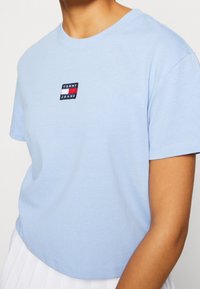 Ljusblå bomull T-shirt med rund hals, korta ärmar och en liten broderad Tommy Jeans-logotyp på bröstet. Slät textur.