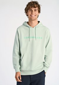 Sudadera verde menta con un bolsillo frontal y cordones. Presenta "COPENHAGUE" impreso en verde claro a lo largo del pecho. Material suave.