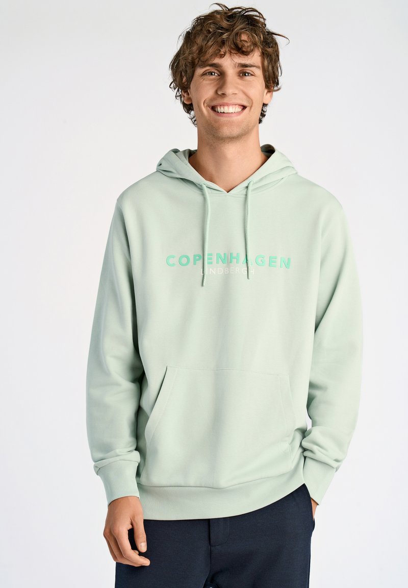 Sudadera verde menta con un bolsillo frontal y cordones. Presenta "COPENHAGUE" impreso en verde claro a lo largo del pecho. Material suave.