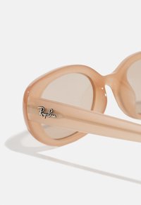 Ochelari de soare Ray-Ban cu rame supradimensionate, rotunde, din plastic piersică deschisă. Lentile întunecate și logo gravat pe temple. Textură netedă.