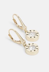 Des boucles d'oreilles à fermoir en or doré présentent un design circulaire avec un centre en pierre précieuse transparente et "DKNY" embouti tout autour.