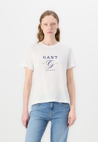 T-shirt di cotone bianco con maniche corte, decorata con un logo stampato blu "GANT EST. 1949 NEW HAVEN" centrato sulla parte anteriore. Collo tondo.