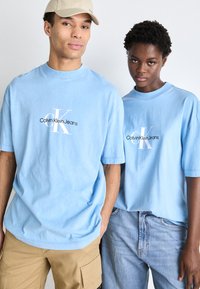Vaaleansiniset puuvillateepaidat, joissa on keskellä logo "Calvin Klein Jeans" musta-valkoisena. Rennon mallinen ja lyhyillä hihoilla.