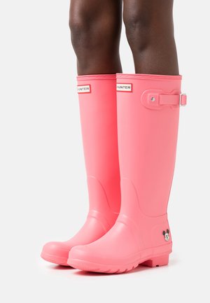Stivali da pioggia in gomma rosa con una finitura lucida, caratterizzati da una fibbia laterale, dettagli con cinturino e un piccolo logo di Topolino sul lato esterno.