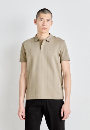 Beige polo shirt featuring a buttoned collar, horizontal stripe texture, and embroidered logo on the chest, paired with black pants.