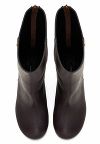Stivali alla caviglia in pelle marrone scuro con una texture liscia, punta arrotondata e pannelli laterali elastici. Presentano un dettaglio con zip dorata sul retro.
