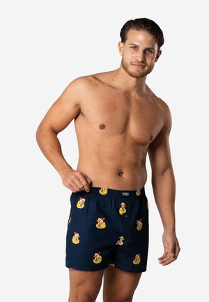 Marineblauwe boxers met een herhalend patroon van gele rubberen eenden die Santa-hots dragen, gemaakt van lichtgewicht stof met een elastische tailleband.
