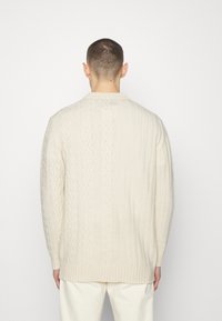 Sweter w kremowym kolorze z dzianiny, z miksami wzorów ściągaczowych i warkoczowych, z okrągłym dekoltem i długimi rękawami.