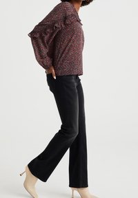 Blusa con motivo floreale e scollo arricciato, abbinata a jeans neri a gamba dritta e scarpe tacchi alti color nude. Tessuto leggero, vestibilità comoda.