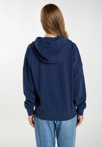 Felpa con cappuccio blu navy a vestibilità rilassata, caratterizzata da polsini e orlo a coste, realizzata in tessuto morbido. Texture liscia, dettagli minimali.