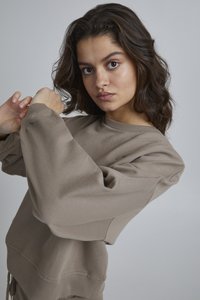 Felpa beige con scollatura a giro, vestibilità ampia e maniche larghe. Realizzata in tessuto morbido, presenta un orlo a coste e cuciture dettagliate.