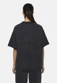 T-shirt oversize grigio scuro con maniche corte. Presenta testo in rilievo e un graffico di una farfalla sul retro. Tessuto morbido.