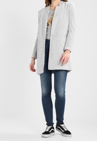 Długi jasnoszary płaszcz z kołnierzem, o prostym kroju i przednimi kieszeniami. Połączony z ciemnoniebieskimi obcisłymi dżinsami oraz czarno-białymi trampkami.