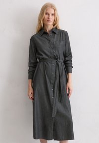 Szara sukienka koszulowa z denimu z paskiem do wiązania, długimi rękawami, zapięciem na guziki i kieszenią na piersi. Tkanina ma miękkie, lekko teksturowane wykończenie.