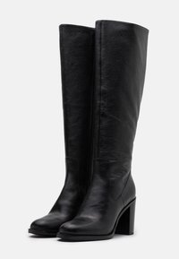 Bottes noires en cuir montant jusqu'au genou, à texture lisse, avec un mollet large et un talon épais. Dotées d'une fermeture éclair latérale.