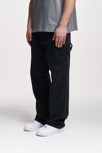 Pantalones de cargo de mezclilla negra con un corte relajado, que cuentan con bolsillos laterales y pasadores para cinturón, complementados con zapatillas blancas.