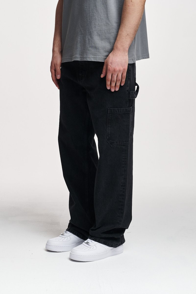 Pantalones de cargo de mezclilla negra con un corte relajado, que cuentan con bolsillos laterales y pasadores para cinturón, complementados con zapatillas blancas.