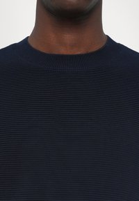 Mørkeblå strikket genser med ribbestruktur og klassisk rund hals. Stoffet ser mykt ut med jevnt fordelte riller.