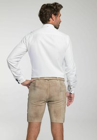 Witte langemouwen shirt en lichtbruine suède shorts met zijzakken. Het shirt heeft een knoopmanchet en een subtiele textuur.